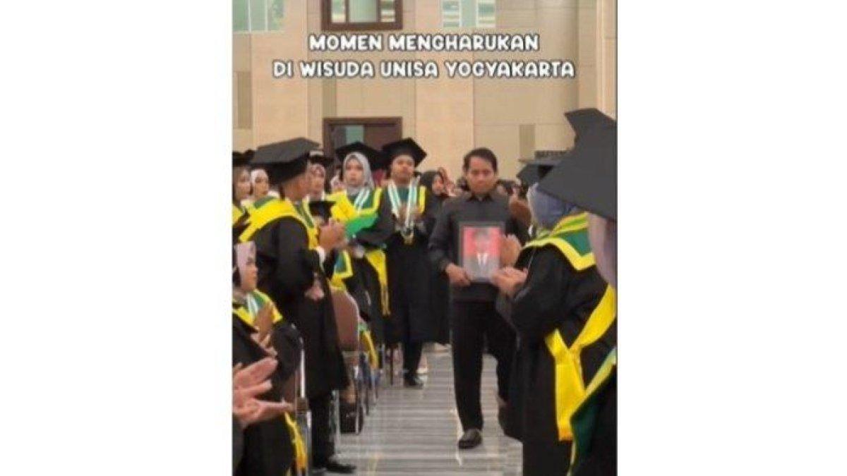 Seorang ayah membawa foto mendiang anak di acara wisuda