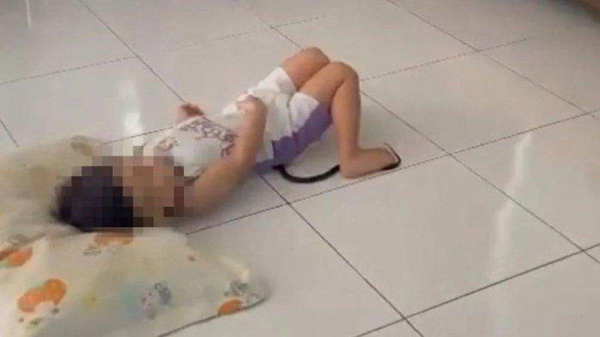 Tangkapan layar video yang memperlihatkan seorang balita di Malaysia tetap tenang dan diam saat ada ular kobra di bawah tubuhnya.