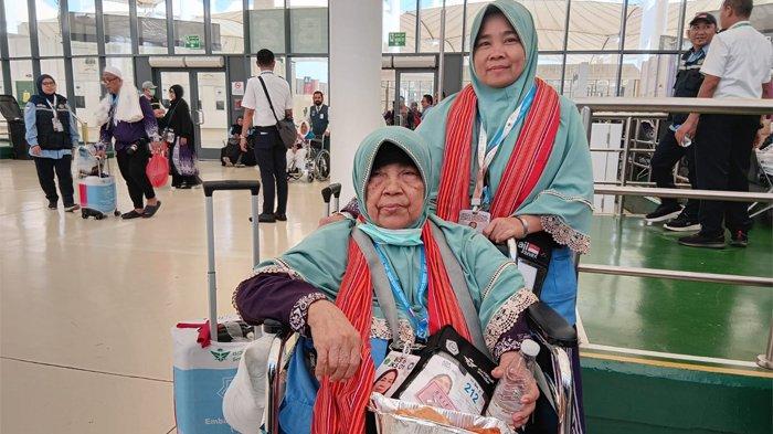 PENDAMPING LANSIA - Erni Istari, jemaah Kloter JKS 01 yang berangkat haji seorang diri ini dengan ikhlas membantu seorang nenek bernama NT Nasihartini yang juga berhaji sendirian tanpa pendamping. Foto diambil Rabu (11/6/2025) saat jemaah kloter JKS 01 hendak kembali ke Tanah Air melalui Bandara Jeddah.