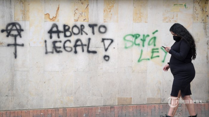 Seorang wanita melewati tembok bertuliskan Aborsi legal dan Itu akan menjadi hukum, selama demonstrasi menunggu keputusan Mahkamah Konstitusi tentang dekriminalisasi di Bogota, pada 18 November 2021. - Orang-orang yang menentang dan mendukung kebebasan aborsi bertemu Kamis ini selama hari protes di depan pengadilan tinggi bahwa minggu ini akan memutuskan apakah akan mendekriminalisasi praktik ini di Kolombia. (Photo by Raul ARBOLEDA / AFP)
