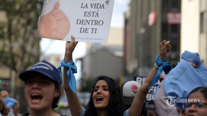 Seorang wanita memegang poster bertuliskan 