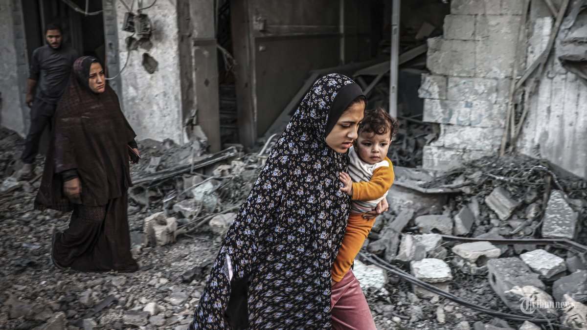 Seorang wanita yang menggendong seorang anak melarikan diri setelah serangan Israel di Rafah di Jalur Gaza selatan pada 23 November 2023, di tengah pertempuran yang sedang berlangsung antara Israel dan kelompok militan Palestina Hamas. (Photo by Mohammed ABED / AFP)