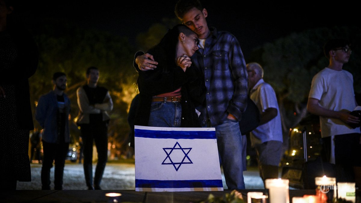 Para peserta berpelukan di samping bendera Israel dan lilin saat acara peringatan untuk para korban Israel di taman Eduardo VII di Lisbon pada 10 Oktober 2023. Pertempuran antara Israel dan Hamas memasuki hari keempat, setelah kelompok militan Palestina melancarkan serangan mendadak besar-besaran dari Gaza yang memicu mobilisasi massa di kedua sisi perpecahan Palestina-Israel. (Photo by Patricia DE MELO MOREIRA / AFP)
