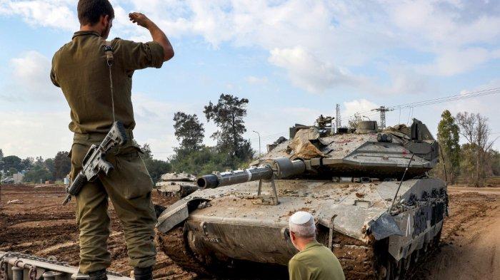 Seorang tentara Israel memberi isyarat agar tank tempur yang mendekat meluncur ke truk trailer di posisi di sepanjang perbatasan dengan Jalur Gaza dan Israel selatan pada 2 Januari 2024, di tengah konflik yang sedang berlangsung antara Israel dan kelompok militan Hamas.