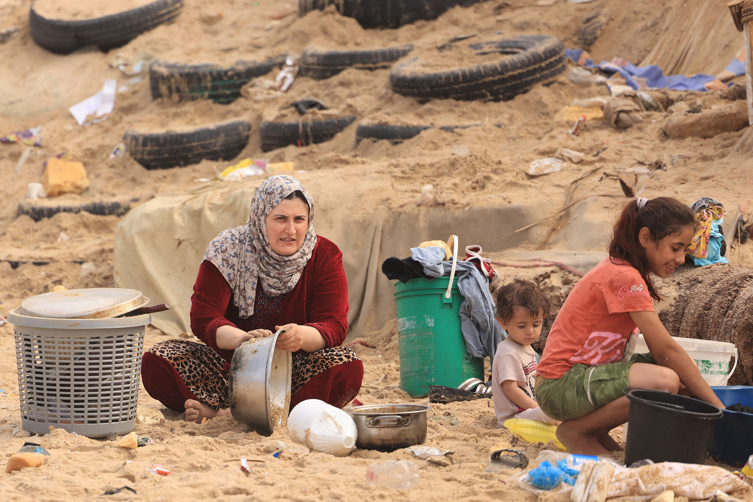 Seorang wanita Palestina membersihkan panci masaknya menggunakan air laut karena kekurangan air bersih dan listrik, di sepanjang pantai di Deir el-Balah di Jalur Gaza selatan pada 29 Oktober 2023, di tengah pertempuran yang sedang berlangsung antara Israel dan kelompok Palestina Hamas . Israel menggempur Gaza yang dikuasai Hamas pada tanggal 29 Oktober, dalam serangan udara dan darat yang meningkat ketika PBB memperingatkan bahwa ketertiban sipil ?mulai rusak? di wilayah Palestina yang terkepung. Ribuan warga sipil, baik warga Palestina maupun Israel, telah tewas sejak 7 Oktober 2023, setelah militan Hamas Palestina yang berbasis di Jalur Gaza memasuki Israel selatan dalam serangan yang belum pernah terjadi sebelumnya yang memicu perang yang diumumkan oleh Israel terhadap Hamas dengan pemboman balasan di Gaza. (Photo by MAHMUD HAMS / AFP)