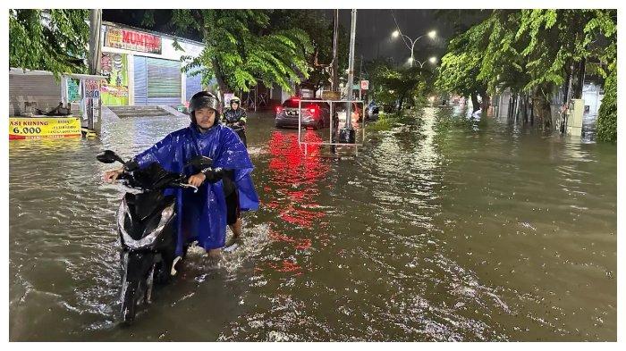 Warga Semarang menuntun motor untuk melewati genangan banjir.