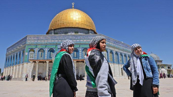 Gadis-gadis Palestina, mengenakan bendera nasional dan hiasan kepala 'kafiyeh' kotak-kotak di depan masjid Dome of Rock di kompleks masjid al-Aqsa di Kota Tua Yerusalem, pada 15 April 2022. Lebih dari 100 orang terluka dalam kekerasan baru. yang terjadi setelah tiga minggu penuh kekerasan mematikan di Israel dan Tepi Barat yang diduduki, dan ketika perayaan Paskah Yahudi dan Paskah Kristen bertepatan dengan bulan suci Ramadhan.