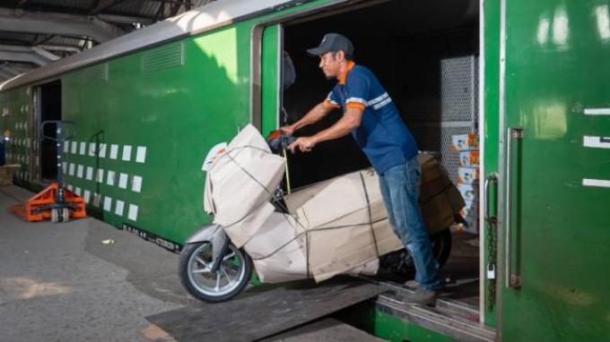 Petugas sedang menurunkan motor yang diangkut ke dalam kereta bagasi.