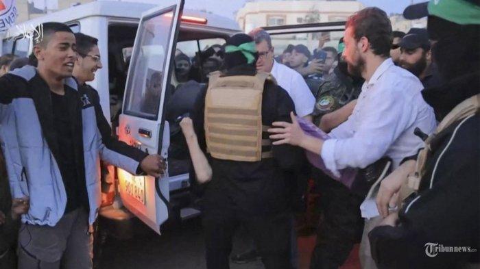 Gambar yang diambil dari video selebaran yang dirilis oleh Kantor Media Hamas menunjukkan seorang anggota Brigade Al-Qassam membawa sandera ke mobil Komite Palang Merah Internasional di Gaza pada 24 November 2023, menjelang pemindahan mereka ke Israel . Setelah 48 hari baku tembak dan pemboman yang merenggut ribuan nyawa, sandera pertama yang dibebaskan berdasarkan kesepakatan gencatan senjata antara Israel dan Hamas diserahkan pada 24 November, kata kedua belah pihak, hampir tujuh minggu setelah mereka ditangkap.