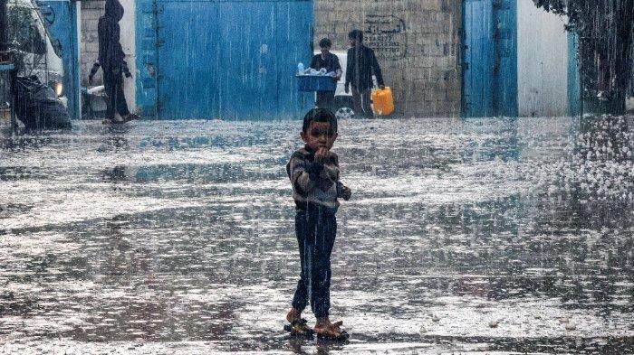 Seorang anak laki-laki berdiri di tengah hujan di sebuah sekolah yang dikelola oleh Badan Bantuan dan Pekerjaan PBB untuk Pengungsi Palestina di Jalur Gaza selatan pada 14 November 2023.